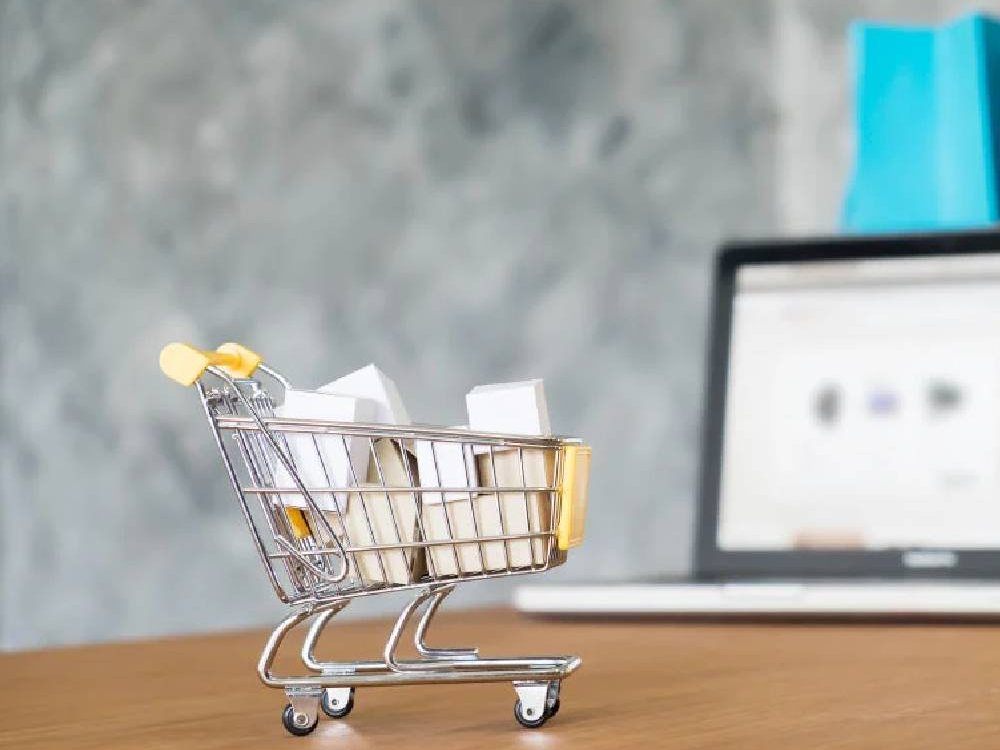 A small shopping cart full of boxes in front of a laptop